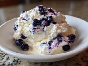 A close-up of a serving of creamy blueberry fluff salad topped with fresh blueberries in a white bowl.