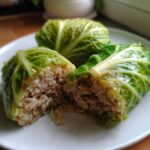Close-up of two cabbage dumplings, one cut open showing the savory filling of ground meat and rice inside the cabbage leaves. These are cabbage dumplings.