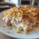 A close-up of a serving of creamy chicken cordon bleu casserole with visible ham chunks and a crunchy breadcrumb topping.
