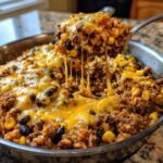 A spoonful of cheesy ground beef and rice skillet being lifted, showing long strings of melted cheese.