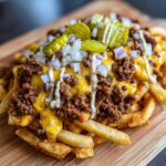 A close-up of loaded cheesy smashburger fries topped with chili, melted cheese, pickles, onions, and sauce.