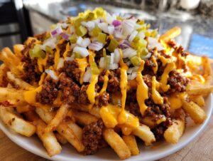 A large serving of cheesy smashburger fries topped with chili, melted cheese sauce, diced onions, and pickles.