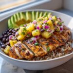 Close-up of a delicious chicken bowl with pineapple salsa, sliced seasoned chicken, brown rice, black beans, and avocado.