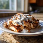 A mound of sliced, grilled chicken shawarma generously topped with creamy garlic sauce on a white plate.