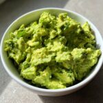 Close-up of chunky, bright green Authentic guacamole mixed with cilantro in a white serving bowl.