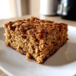 Close-up of a moist square slice of cinnamon baked oatmeal sheet cake with a crunchy topping on a white plate.