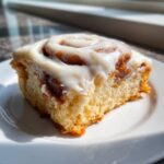 A single, square portion of soft cinnamon roll bars topped generously with thick cream cheese frosting.