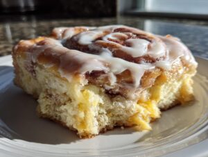 A close-up of a single square cut from cinnamon roll bars, generously topped with white cream cheese frosting.
