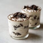 Two servings of creamy cookies and cream mousse layered with crushed chocolate cookies in clear glasses.