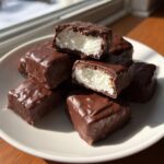 A stack of homemade cool whip candy bars covered in rich chocolate, with two pieces cut open showing the white filling.