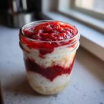 Close-up of layered cottage cheese strawberry cheesecake chia seed pudding in a small glass jar.