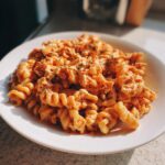 A white plate filled with creamy, orange-hued baked feta pasta mixed with fusilli noodles and herbs.