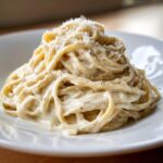 A close-up of creamy spaghetti coated in cottage cheese alfredo sauce, topped with grated Parmesan.