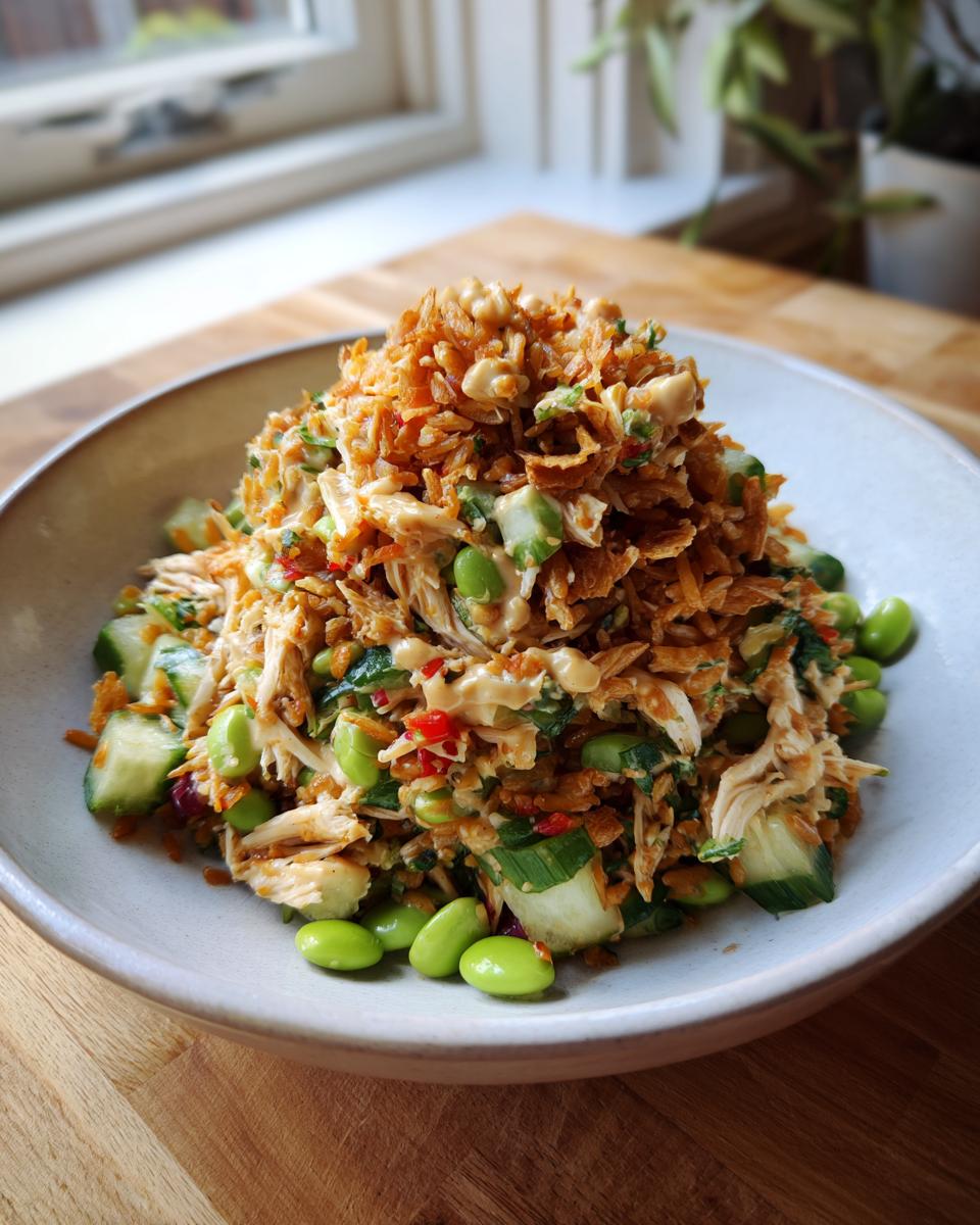 A bowl filled with vibrant crispy rice salad featuring shredded chicken, cucumber, edamame, and topped with crunchy fried rice.