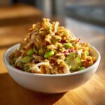 A close-up of a generously portioned crispy rice salad topped with fried onions, bright green edamame, and a creamy dressing.