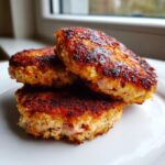 A stack of three golden-brown, crispy salmon cakes resting on a white plate.
