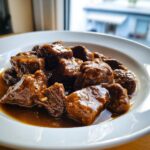 Close-up of tender, glossy crockpot beef tips swimming in a rich brown sauce served in a white bowl.