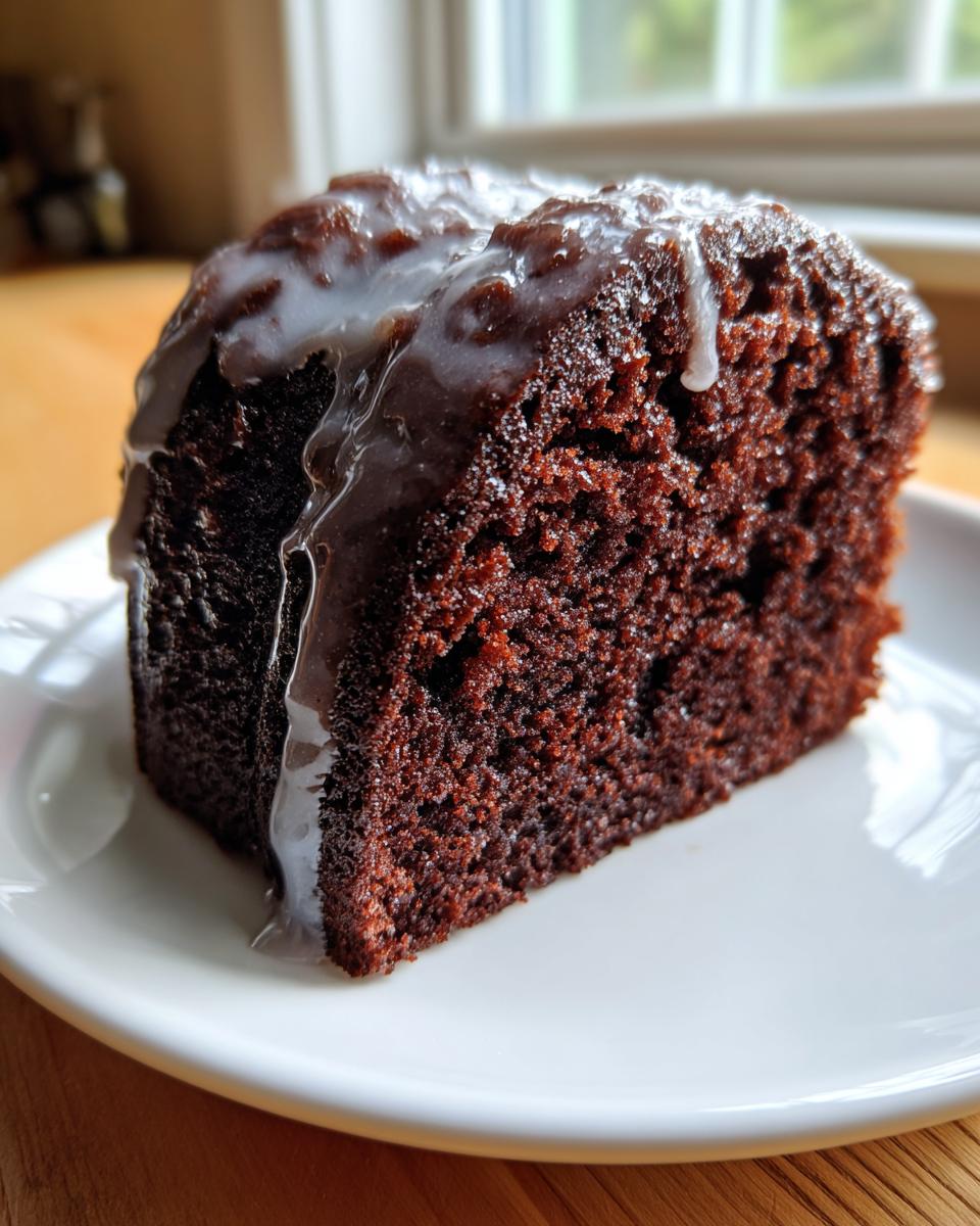 Close-up of a rich, dark slice of Dr Pepper cake topped with a thin white glaze dripping down the side.