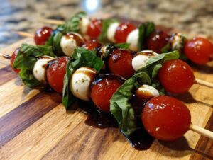 Close-up of freshly made caprese skewers featuring cherry tomatoes, mozzarella balls, basil, and balsamic glaze.