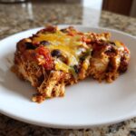 A close-up serving of cheesy fajita chicken casserole with shredded chicken, black beans, and peppers on a white plate.