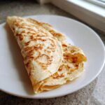 A folded, lightly browned cottage cheese wrap served on a white plate, ready to be filled.