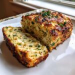 A golden-brown slice cut from a loaf of garlic parmesan chicken meatloaf, topped with fresh parsley.