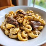 A close-up of creamy garlic steak tortellini tossed in a rich sauce and topped with red pepper flakes.