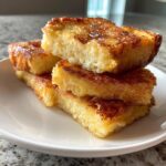 A stack of three golden-brown Hawaiian Roll French Toast pieces drizzled with syrup on a white plate.