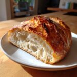 A close-up of a freshly baked homemade ciabatta loaf cut in half, showing its airy, open crumb structure and golden crust.