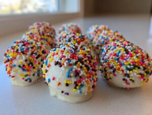 A close-up of several homemade white chocolate starbucks cake pop treats generously covered in colorful rainbow sprinkles.
