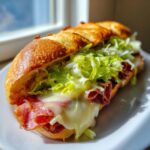 Close-up of a delicious Italian hoagie sandwich on a crusty roll with melted cheese, deli meats, and shredded lettuce.