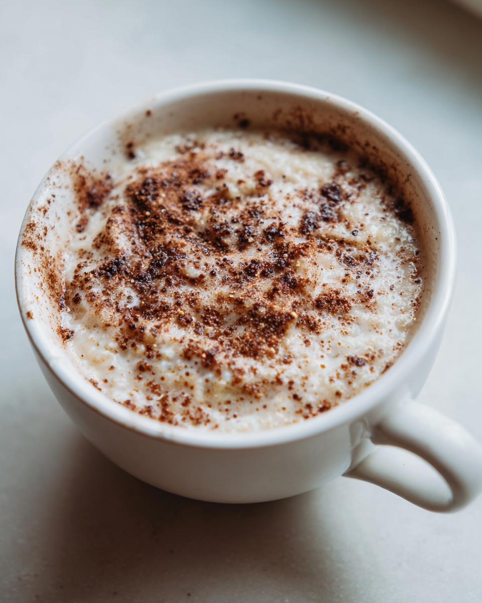 Close-up of creamy jamaican cornmeal porridge with coconut milk, topped with sprinkled cinnamon or nutmeg.