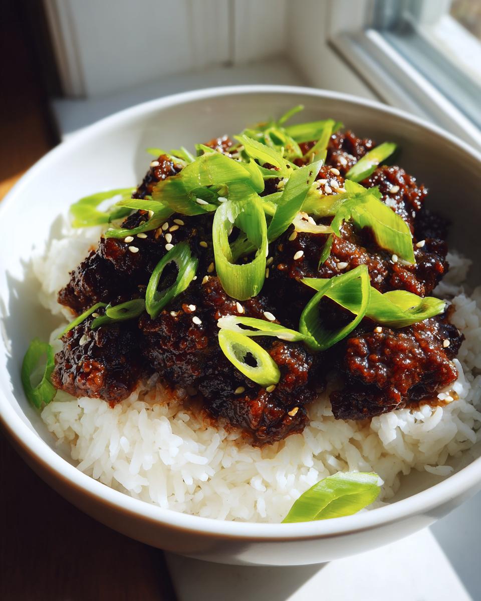 Close-up of a korean ground beef bowl featuring rich, dark sauce over white rice, topped with sliced green onions and sesame seeds.