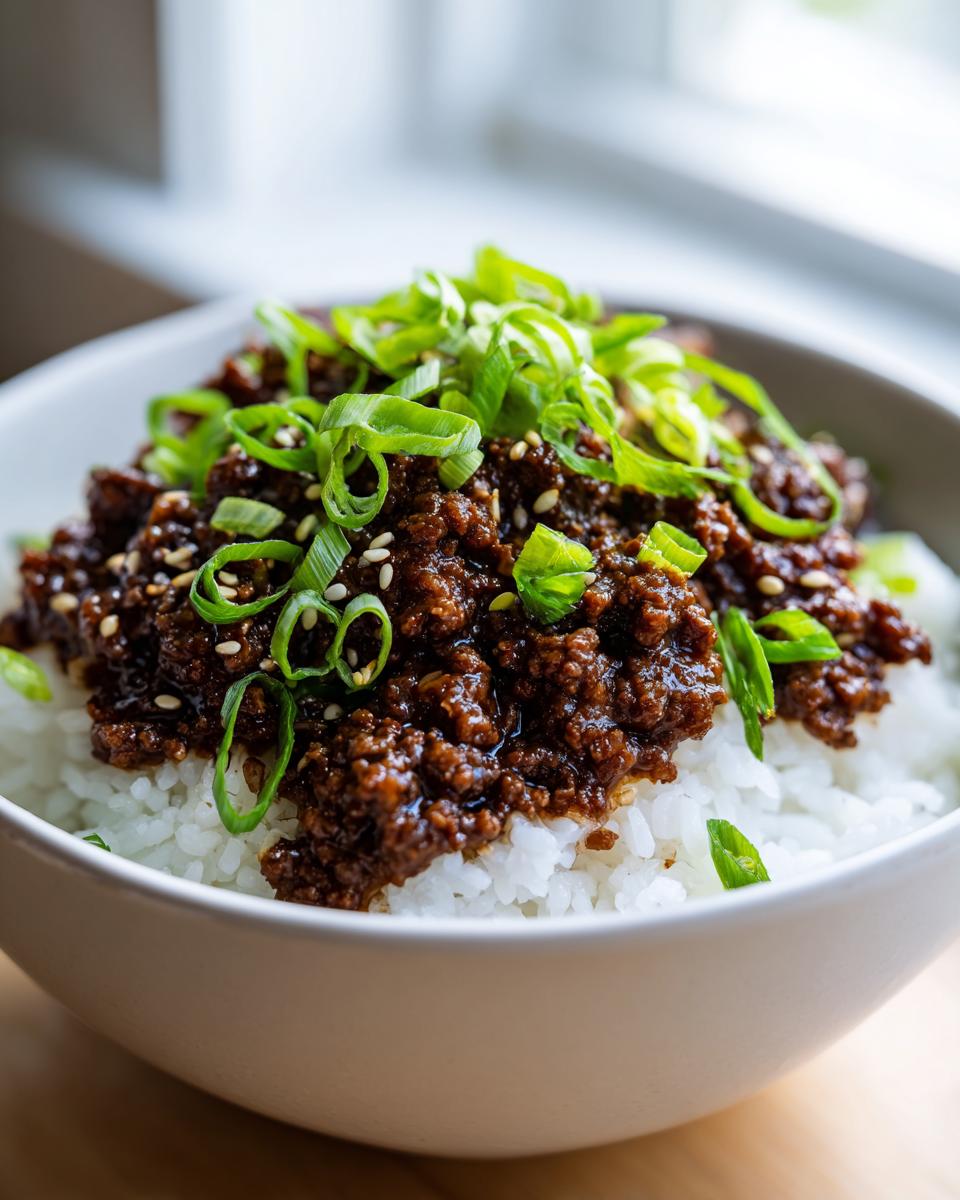 A close-up view of a korean ground beef bowl featuring saucy ground beef over white rice, topped generously with sliced green onions and sesame seeds.