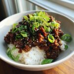 A close-up of a korean ground beef bowl featuring savory ground beef over white rice, topped with sliced green onions and sesame seeds.