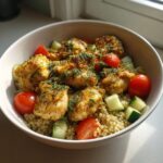 A close-up of a vibrant lemon dill chicken bowl featuring seasoned chicken pieces over quinoa, mixed with cherry tomatoes and cucumber.