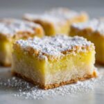 A close-up of a square Margarita bars slice, featuring a bright yellow-green filling and a crumbly topping dusted heavily with powdered sugar.