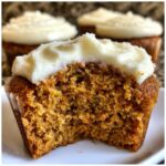Close-up of a carrot cake cupcakes cut in half showing the moist crumb and thick cream cheese frosting.