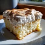 A close-up, sunlit slice of moist Tres leches cake topped with fluffy whipped cream and a dusting of cinnamon.