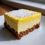 Close-up of a single serving of no-bake lemon bars showing a thick graham cracker crust and creamy lemon filling topped with powdered sugar.
