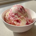 A generous scoop of swirled white and pink no-churn strawberry kefir ice cream in a white bowl.