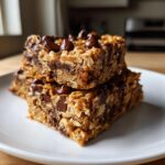 Two stacked oatmeal chocolate chip peanut butter bars topped with melted chocolate chips on a white plate.