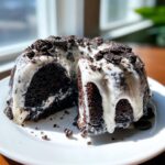 Close-up of a rich, dark chocolate Oreo bundt cake slice covered in white glaze and cookie crumbs.