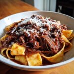 Close-up of wide pappardelle pasta topped generously with shredded beef ragu and grated Parmesan cheese.