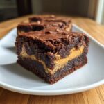 A rich, fudgy square of peanut butter stuffed brownies showing the creamy peanut butter layer inside.
