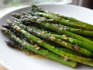 Close-up of bright green roasted asparagus spears seasoned with garlic and oil on a white plate.