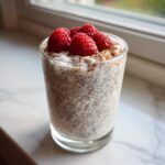 A glass of creamy chia seed pudding topped with fresh raspberries and a sprinkle of cinnamon.