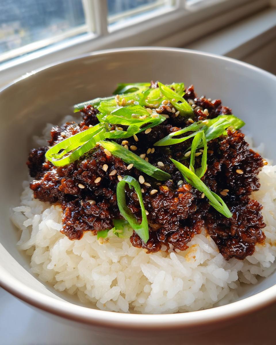 Close-up of a korean ground beef bowl featuring savory dark ground beef over white rice, topped with fresh green onions and sesame seeds.
