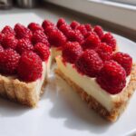 Two slices of a creamy Raspberry Tart topped generously with fresh, bright red raspberries on a white plate.