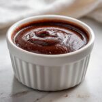 A close-up of rich, dark Chocolate custard filling a small white fluted ramekin.